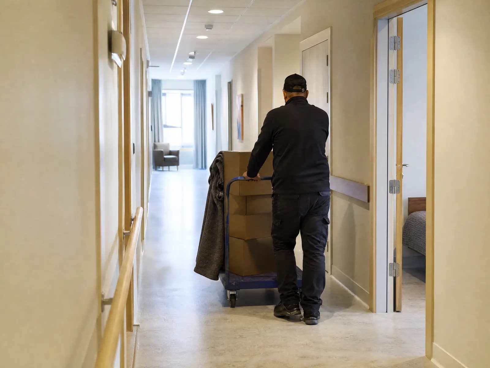 Opruimer rijdt een trolley met gesloten dozen door de gang van een woonzorgcentrum